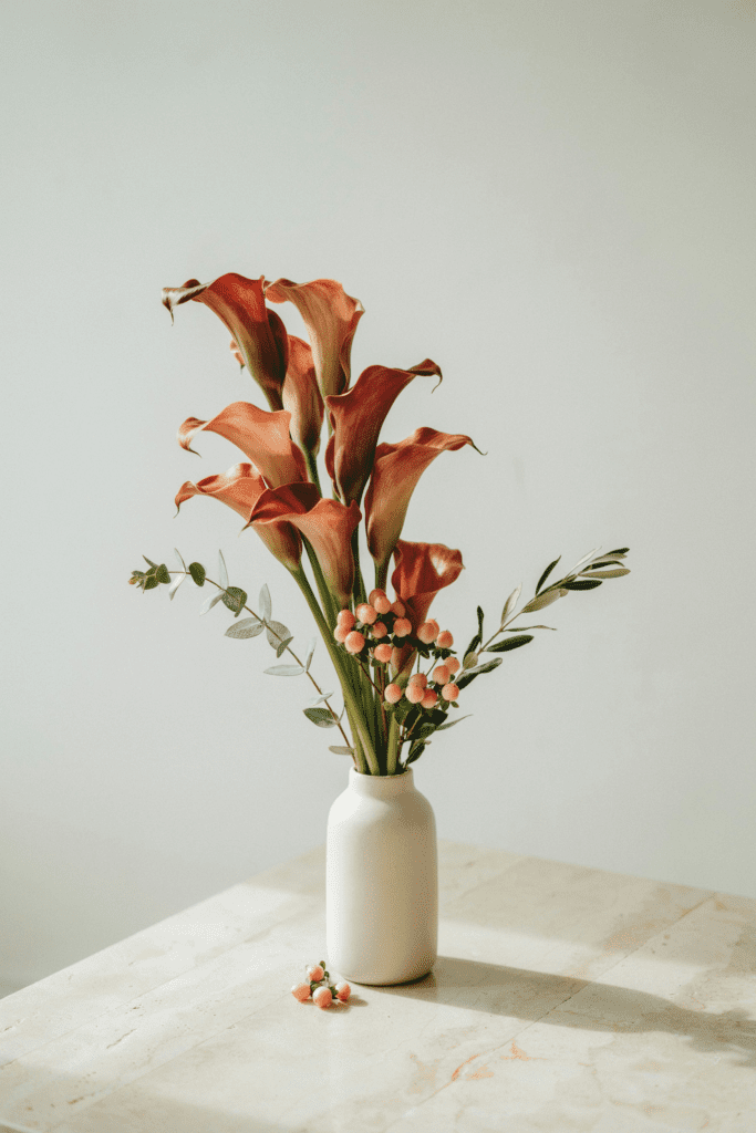 Modern, architectural bouquet of deep burnt orange calla lilies with peach hypericum berries and minimal greenery