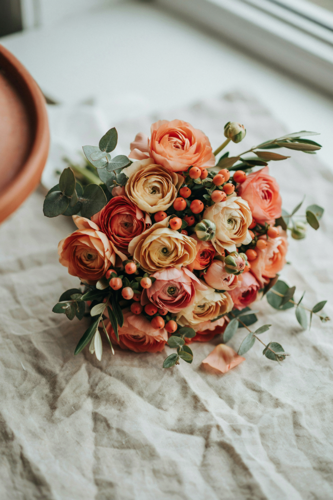 Romantic, full bouquet of apricot ranunculus layered with terracotta hypericum berries and soft greenery