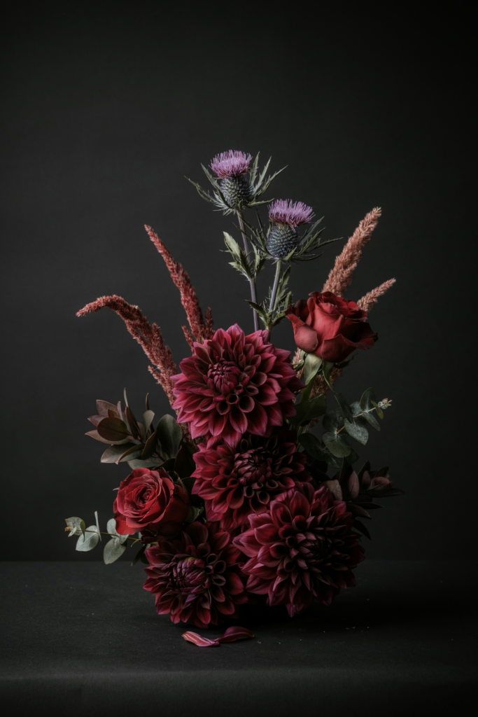 Dark, architectural bouquet of eggplant dahlias, burgundy roses, purple thistle flowers, and reddish-brown sorghum stems