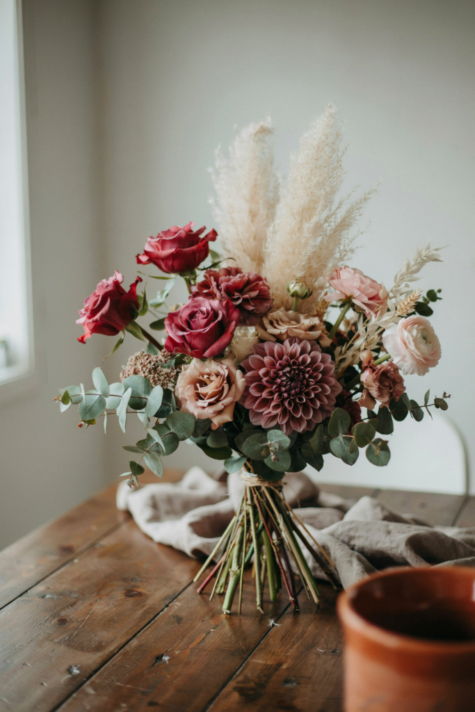 Eclectic, textural bouquet mixing burgundy roses, plum dahlias, blush ranunculus, and feathery dried pampas grass