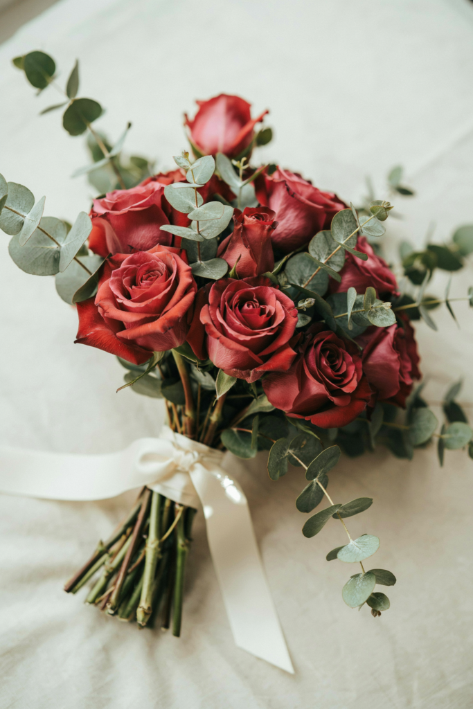  Close-up of a hand-tied bouquet of deep burgundy garden roses with silver dollar eucalyptus, tied with ivory satin ribbon