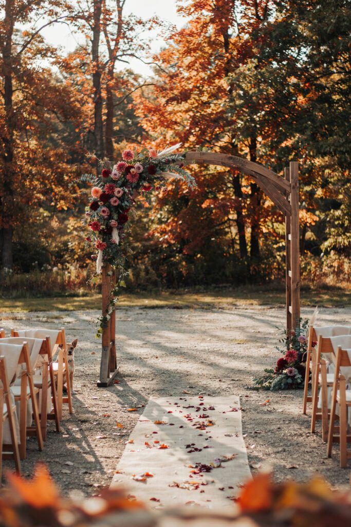  A wooden arch completely covered in thick green moss with cascading wildflowers — ranunculus, sweet peas, and Queen Anne's lace — spilling from the top corners, photographed in soft afternoon light