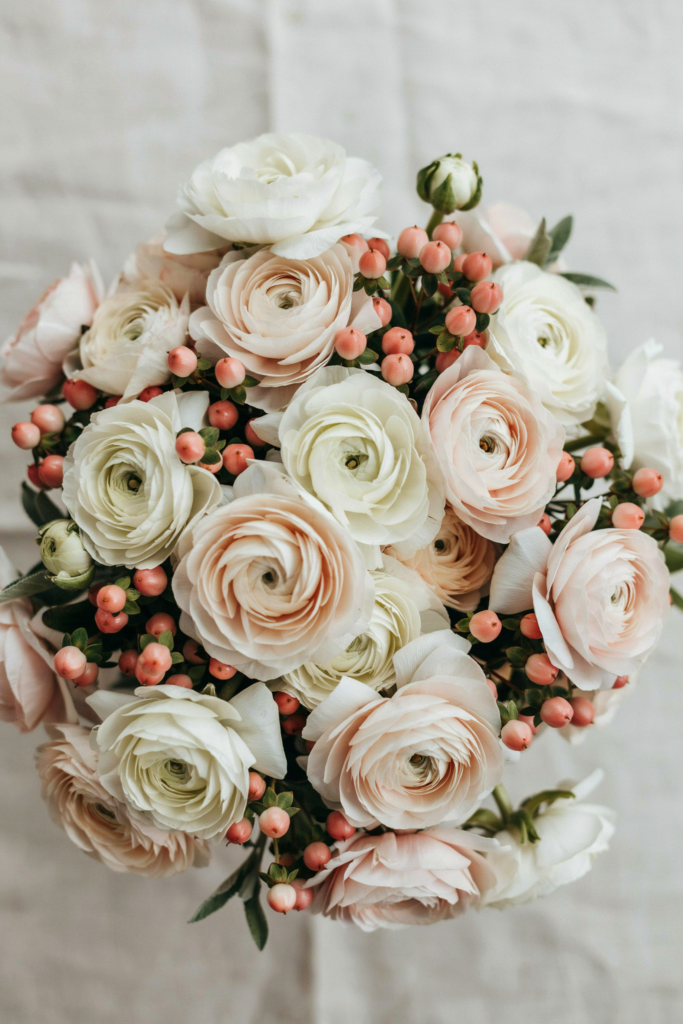 Full, textural bouquet of densely packed ivory ranunculus with blush hypericum berries throughout