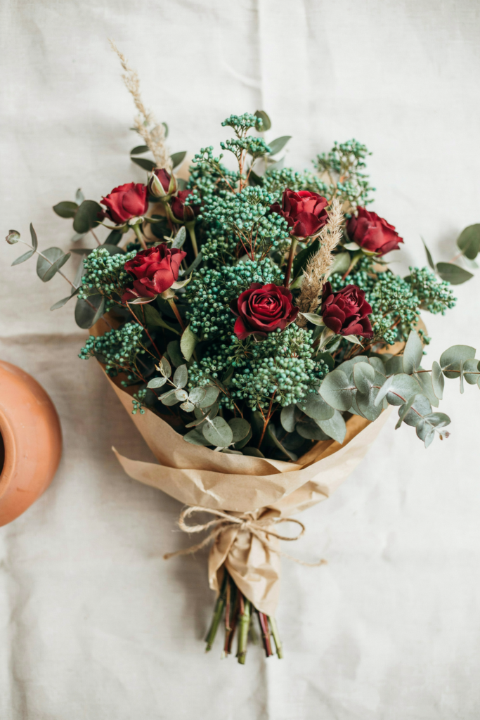 Modern, textural bouquet of small teal brunia berries mixed with burgundy roses and silver eucalyptus