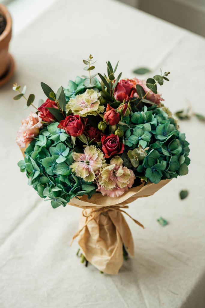 Sophisticated, layered bouquet of emerald hydrangea, burgundy roses, and green trick dianthus