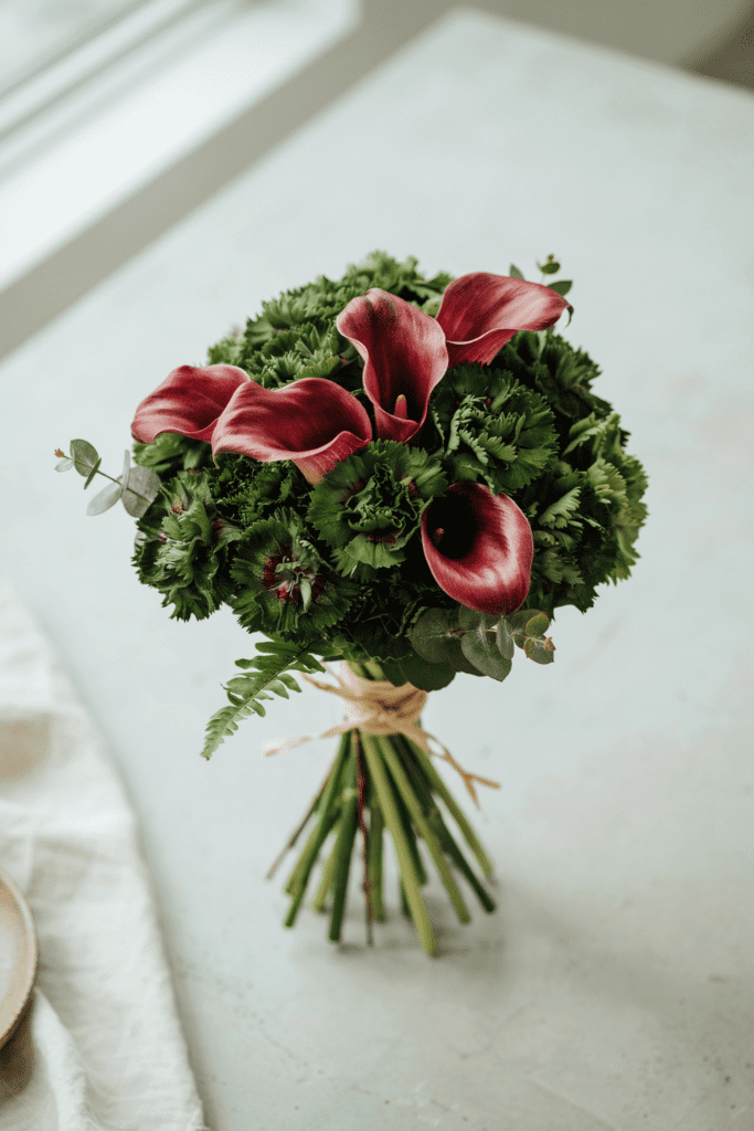 Compact, modern bouquet of deep forest green trick dianthus mixed with burgundy calla lilies