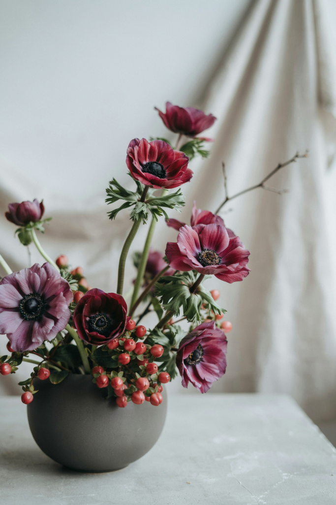 Modern, sculptural bouquet of deep plum anemones with dark centers, mixed with burgundy hypericum berries