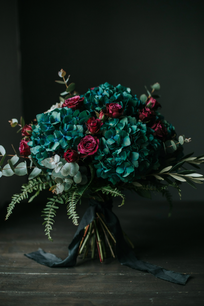 Lush, dramatic bouquet of deep emerald hydrangea clustered with burgundy roses and trailing greenery