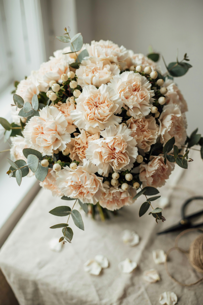 Full, voluminous bouquet of cream carnations clustered with ivory hypericum berries and silvery seeded eucalyptus