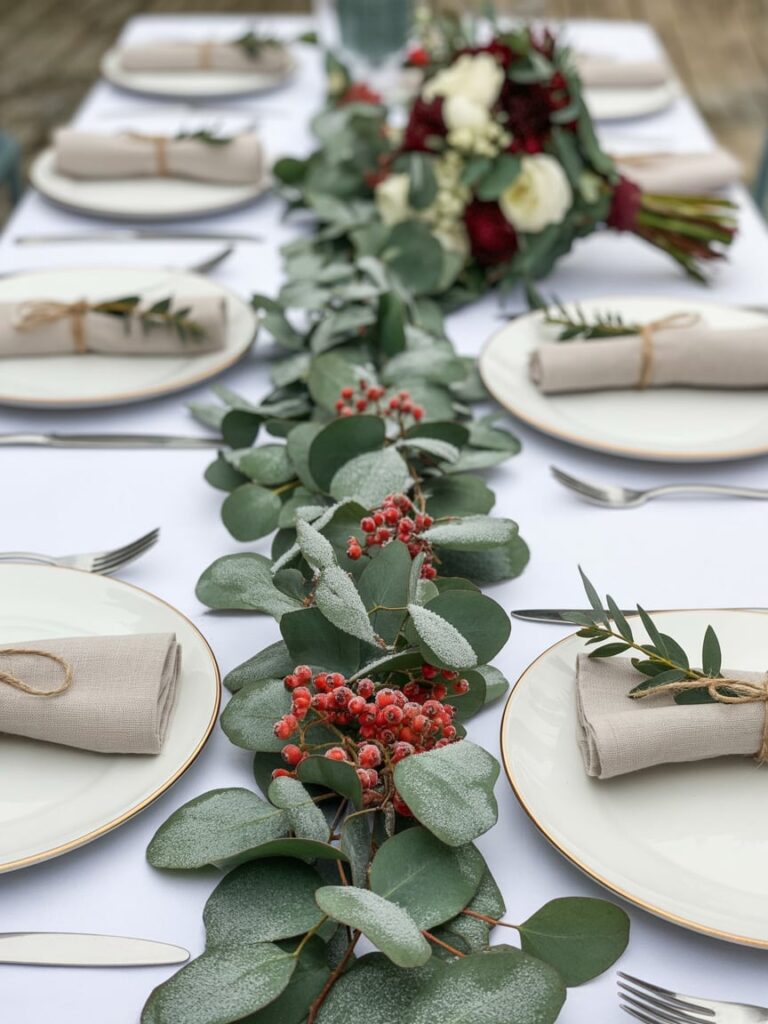 Winter wedding table runner made of frosted eucalyptus and red berries with linen napkins tied with twine and handwritten name tags.