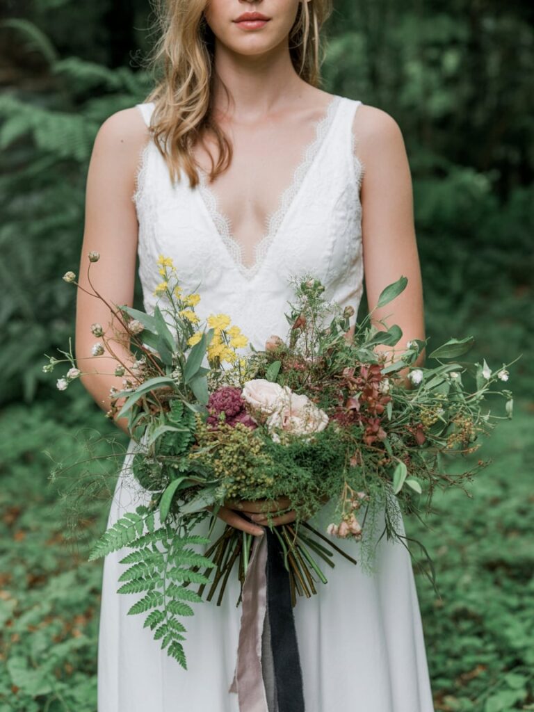 Organic forest wedding florals with loose greenery, ferns, wildflowers, and garden roses, natural movement and texture, hand-tied bouquet style, romantic and airy composition, high-end wedding editorial photography