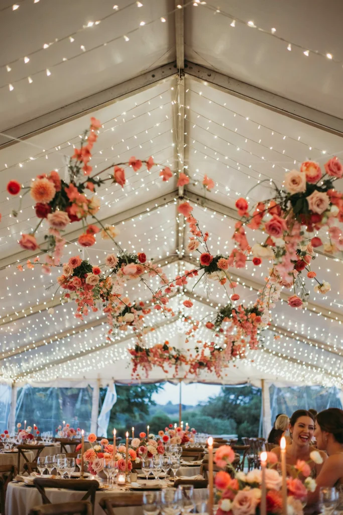 A tented outdoor reception space with thousands of warm white fairy lights overhead and pink floral garlands draped between the light strings, creating a ceiling of light and flowers