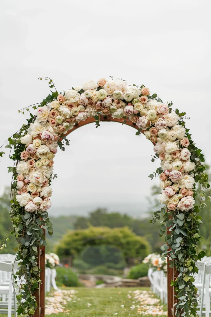  A ceremony arch covered in full-bloom blush peonies and ranunculus, with cascading eucalyptus and ivy trailing toward the ground