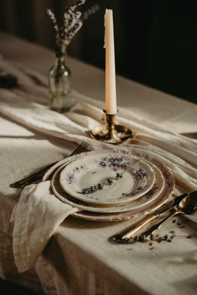 Mismatched vintage floral china plates in ivory and lavender tones stacked at each place setting with a linen napkin and single stem