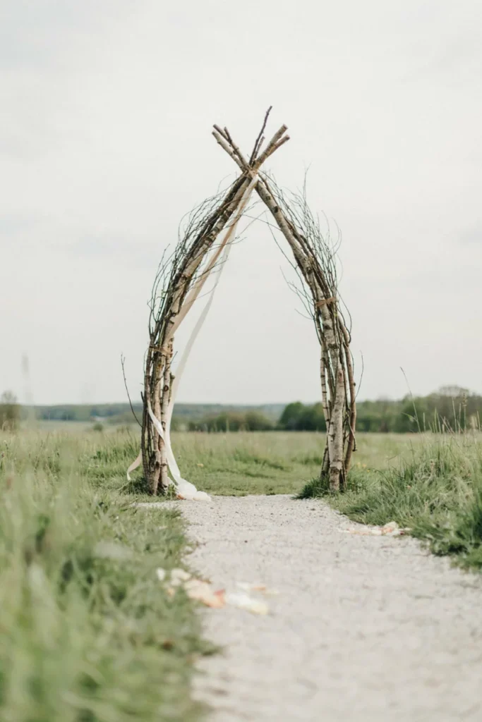 Minimalist bare branch archway with a single trailing ivory ribbon at a winter wedding aisle