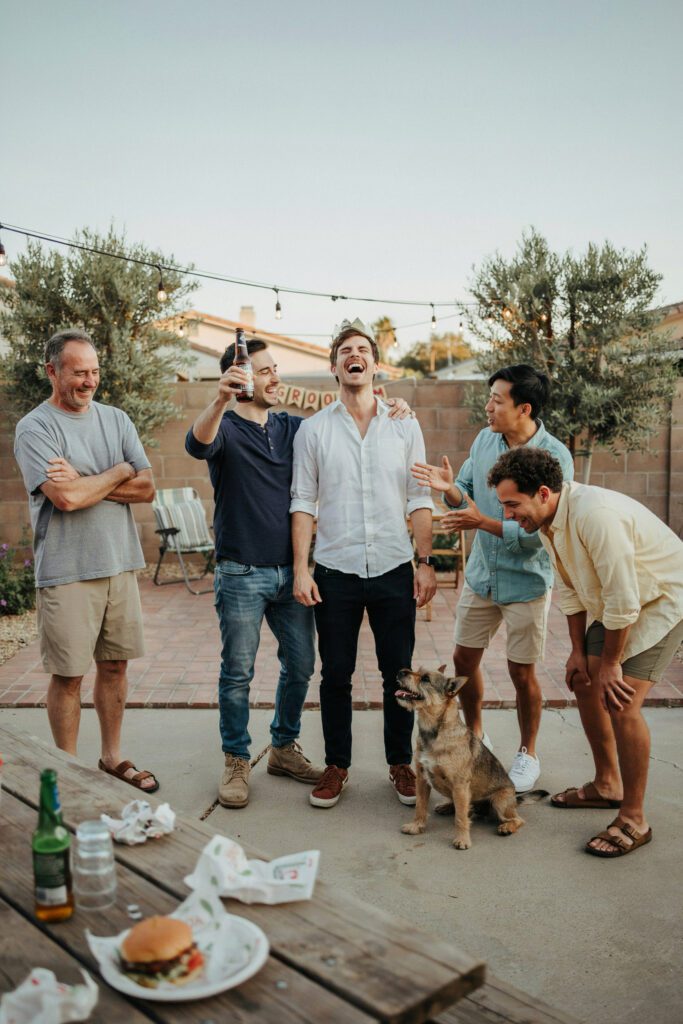 A group of men laughing and celebrating at a casual outdoor gathering — representing a relaxed, fun bachelor party setting.