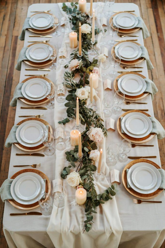 An overhead shot of a small, beautifully set reception table with candles, greenery, and place settings for about 20 guests — warm and elegant