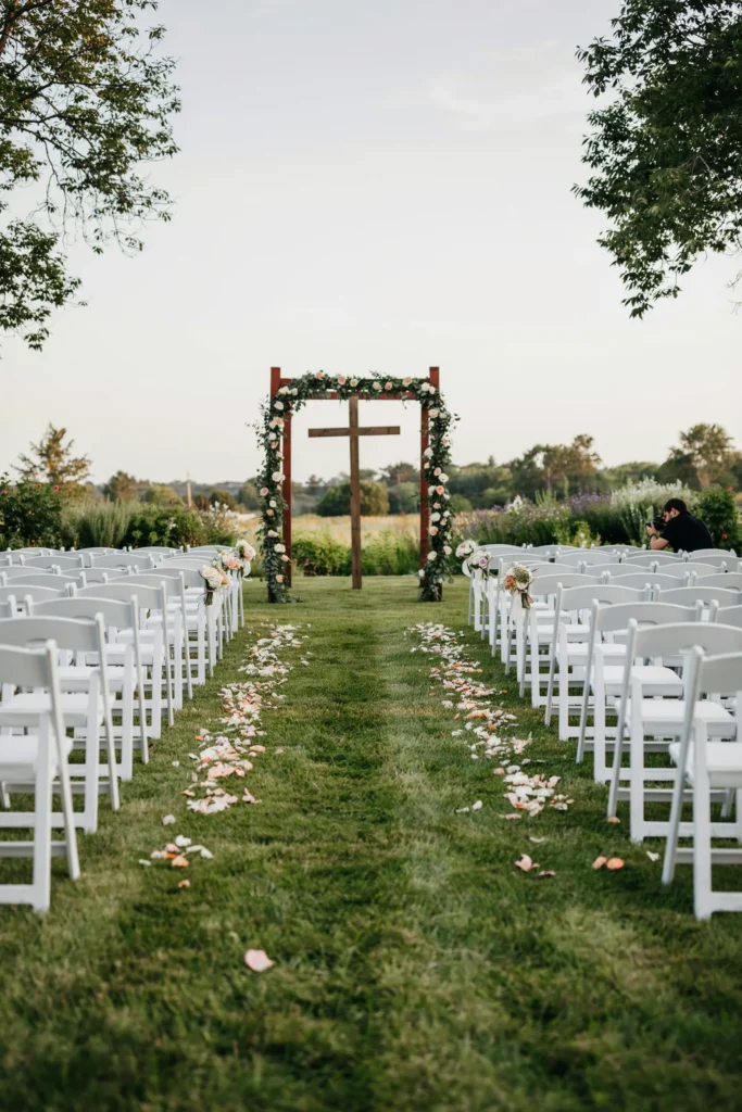 Rows of crisp white folding chairs arranged in a gentle curve facing a barn altar, with a narrow petal-strewn aisle down the center