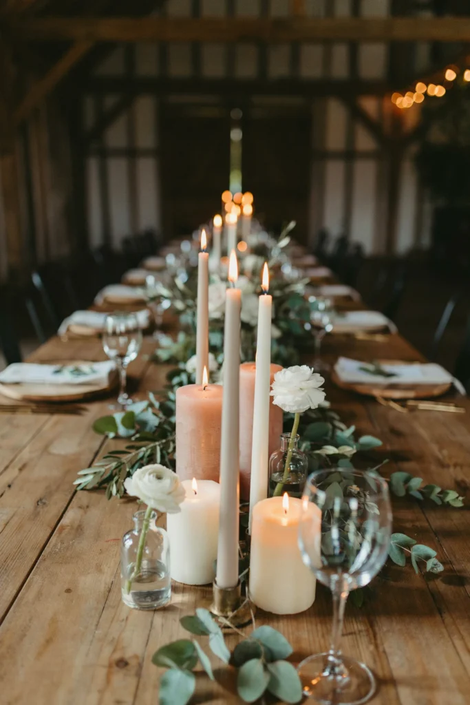Clusters of varying-height flameless pillar candles grouped at the center of a long wooden reception table
