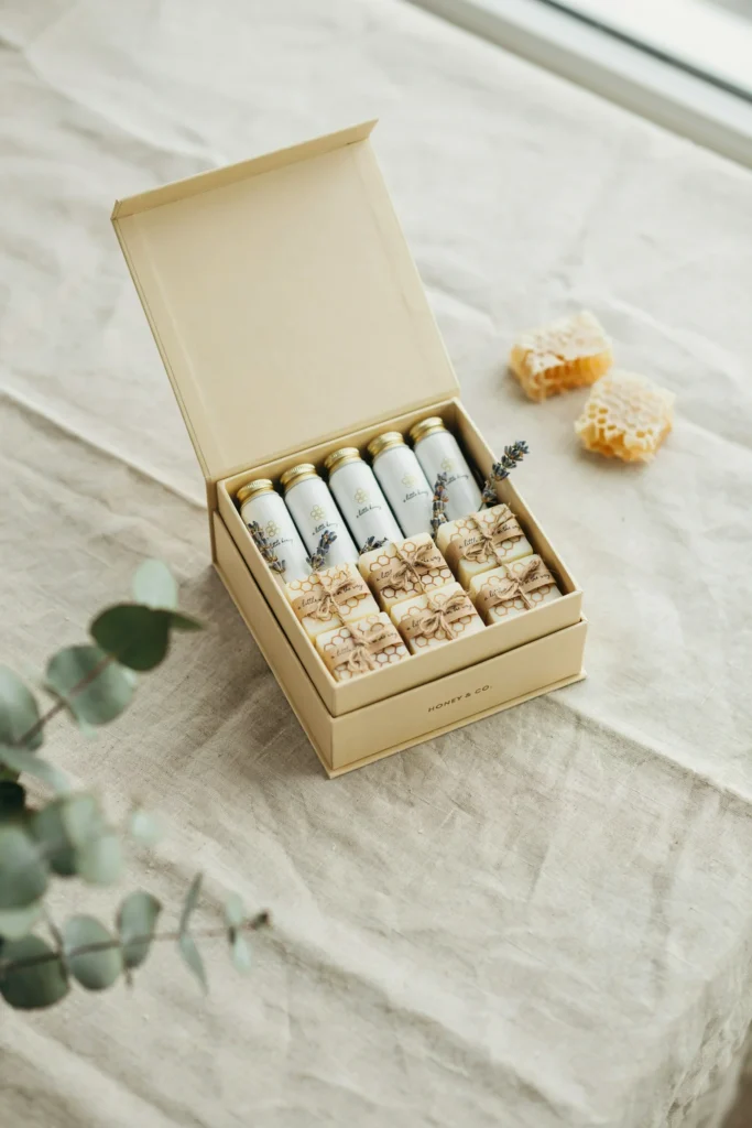 A favor display of small honeycomb-printed soap bars and hand cream tubes, each labeled "a little honey is on the way," arranged in a gold gift box.