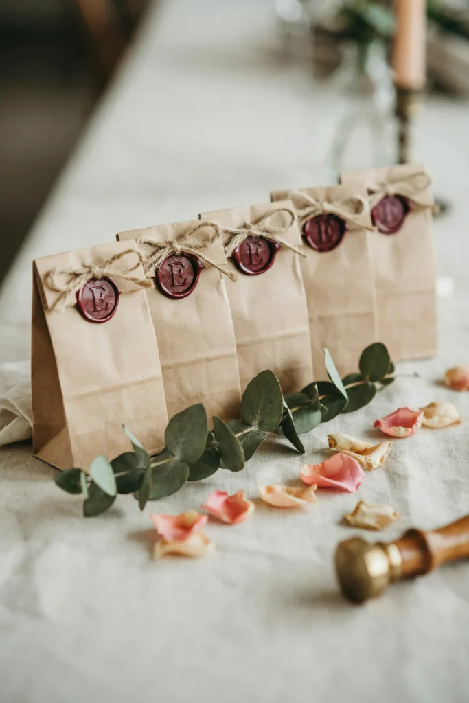 A row of small favor bags or boxes tied with twine, each finished with a small wax seal stamp pressed directly onto the knot, the bride's monogram visible in the wax.