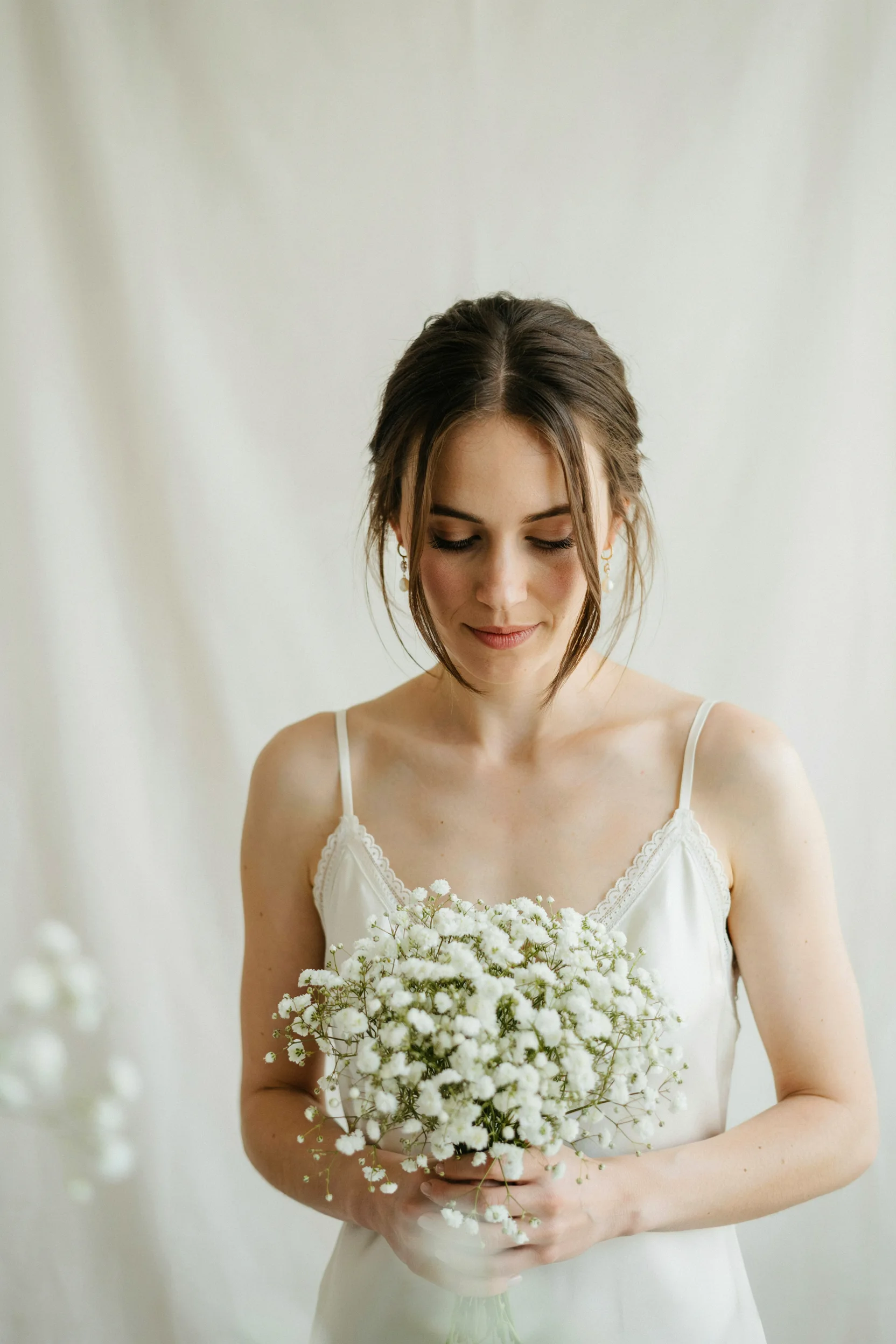 A bride holding a full, cloud-like all-white baby's breath bouquet against a soft neutral backdrop, natural light, romantic and airy mood.