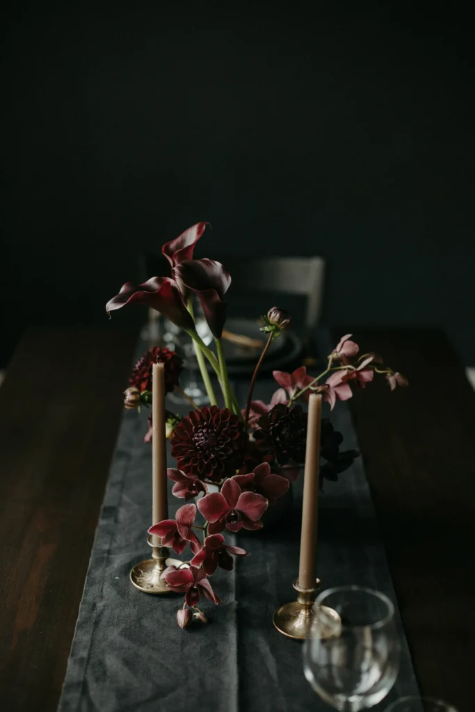 A centerpiece of deep burgundy-black calla lilies, dark dahlias, and near-black orchids against a matte black table runner