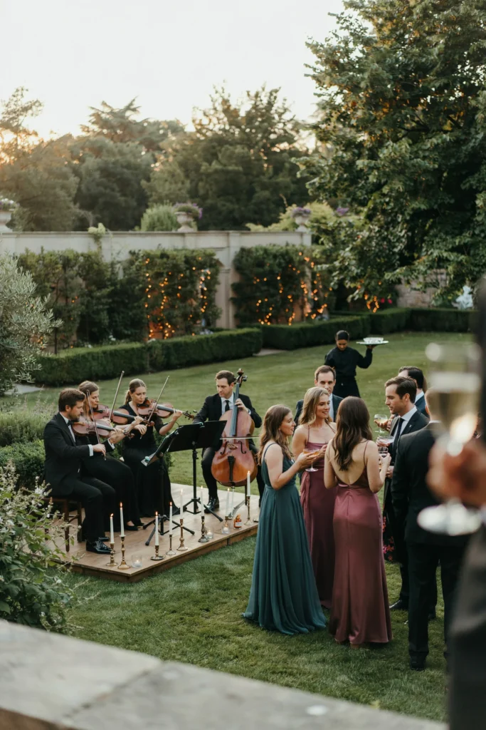 A four-piece string quartet performing during an outdoor cocktail hour, guests mingling in formal attire in the background