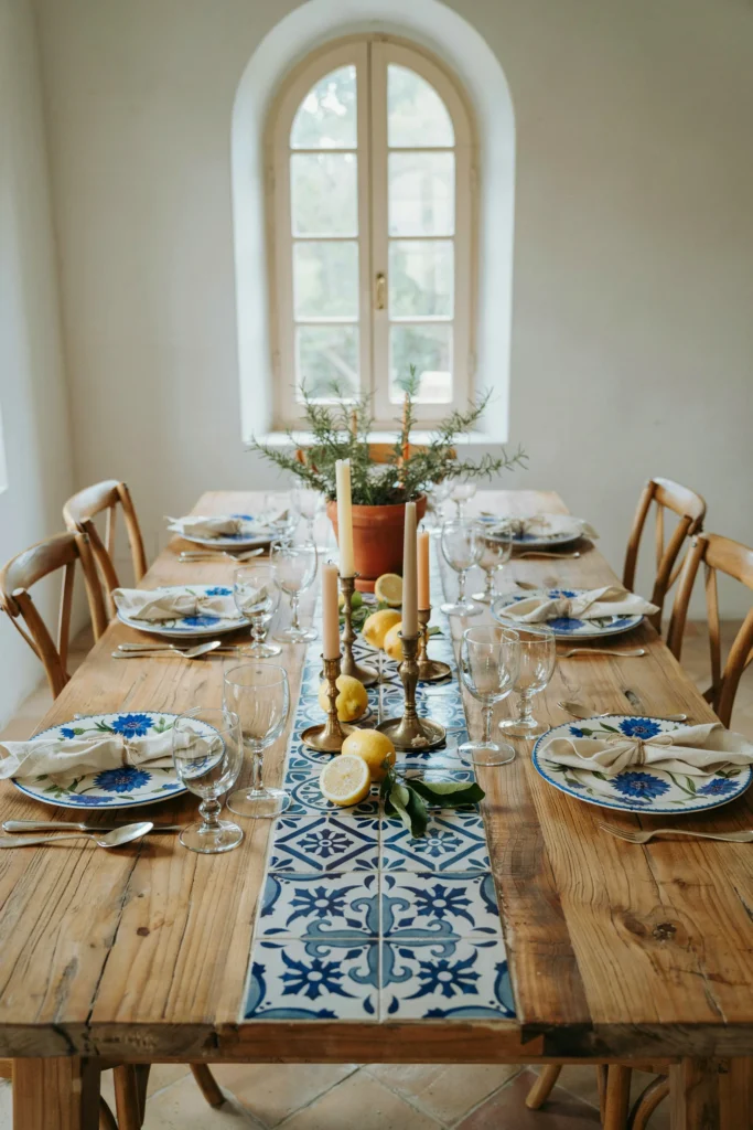 Long dining table styled with a blue-and-white tiled table runner, fresh lemons scattered between place settings, and coordinating blue floral plates.