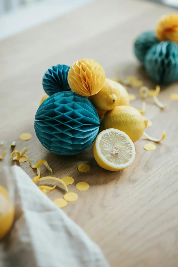  A cluster of blue and yellow honeycomb paper centerpieces arranged with fresh lemons and scattered lemon confetti on a tabletop