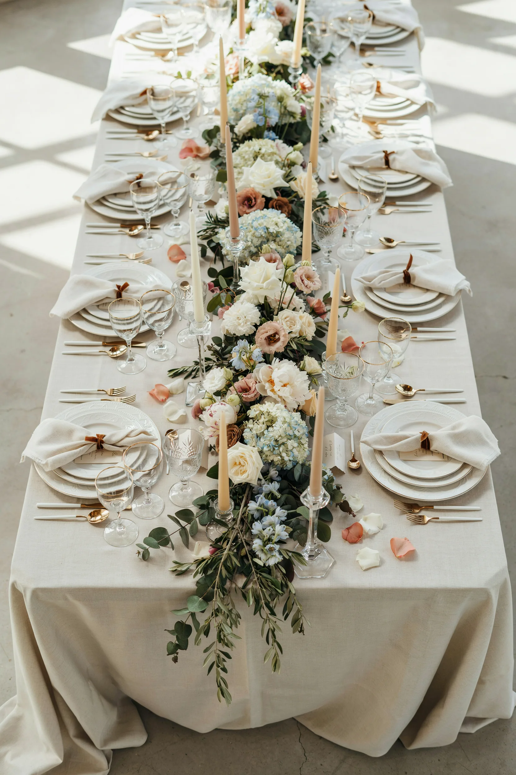 An overhead shot of a reception table dressed in a lush floral runner with mixed candle heights, soft natural light, no text overlay needed — let the flowers speak