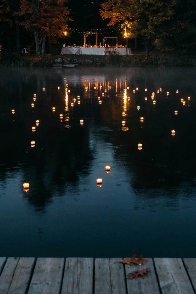 Dozens of floating candles glowing across a still dark lake at night near a wedding reception