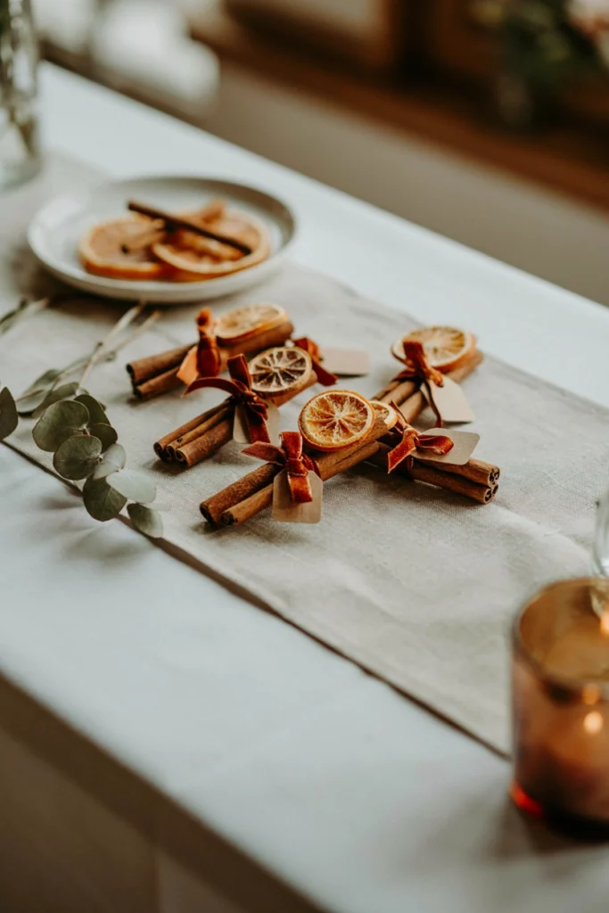 Cinnamon stick wedding favor bundles tied with rust twine and dried orange slices on a burlap runner