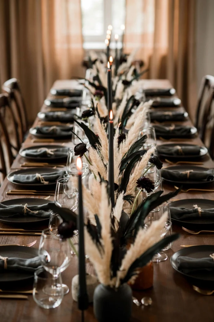 Long wedding banquet table runner made of black feathers and pale pampas grass with black taper candles