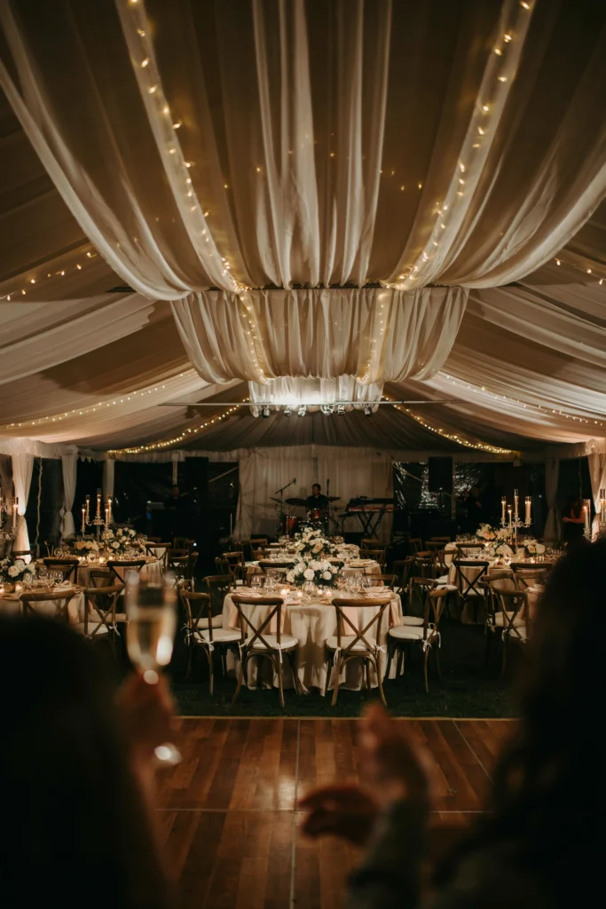Reception tent ceiling fully draped in champagne silk fabric, softly lit from below