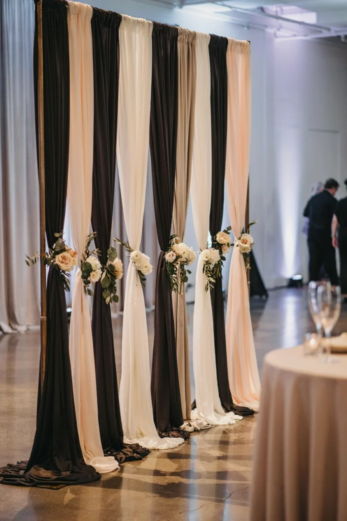 Wedding reception backdrop made of alternating black and ivory fabric swags with small floral clusters