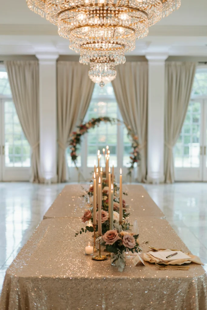 Reception table draped in shimmering champagne sequin linen beneath a crystal chandelier