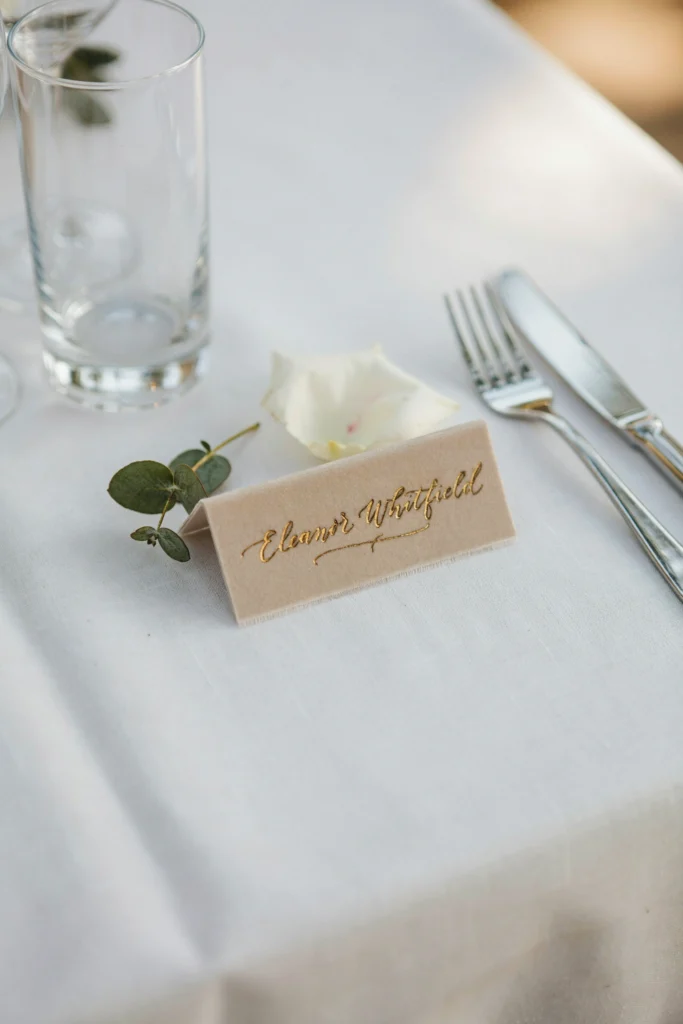 Champagne velvet ribbon place card hand-lettered in gold ink, folded on a table setting