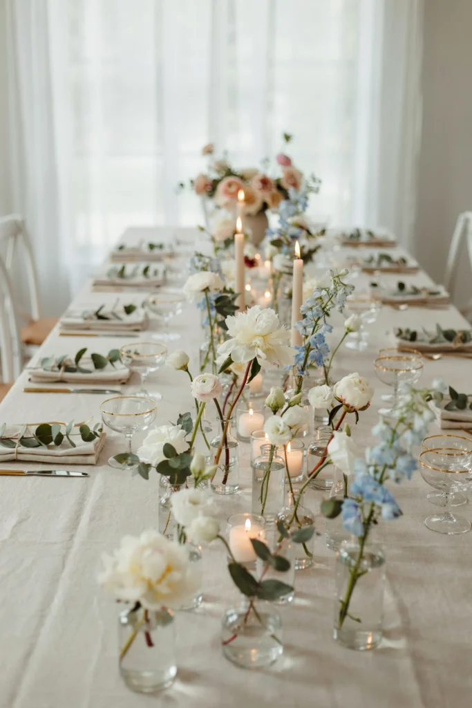 Small glass bud vases with single stems scattered along a bridal shower table