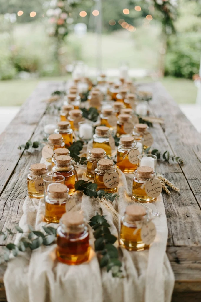 Mini glass honey jars with round kraft labels tied with twine on a wood table, an edible wedding favor idea