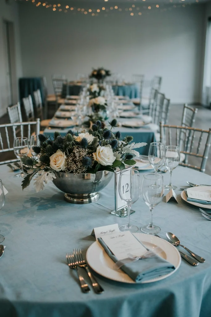 Dusty blue thistle and white rose centerpiece in a silver bowl