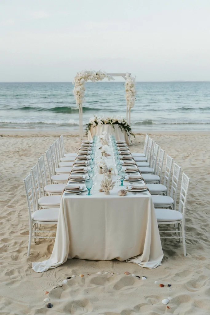 Coral and shells scattered among candles and white linens on a beach table