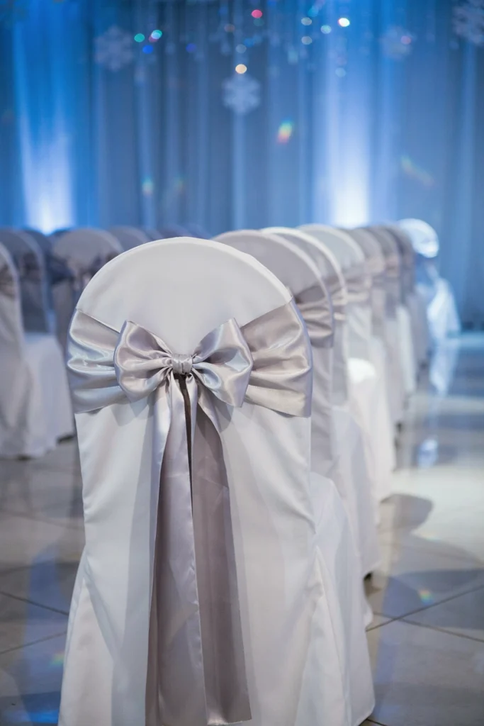 White wedding chairs tied with shimmering silver sash bows