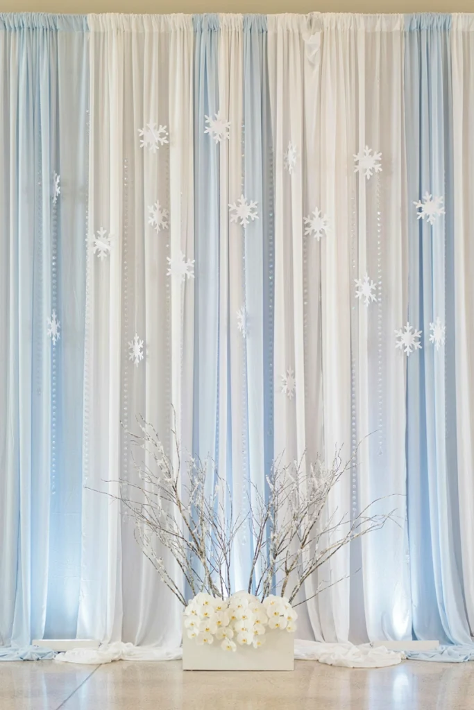 Sheer white curtain ceremony backdrop with suspended paper snowflakes