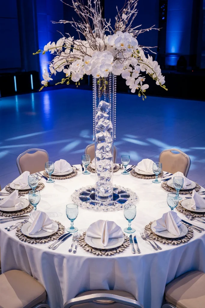 Wedding tablescape with a tall glass cylinder crystal centerpiece and silver charger plates