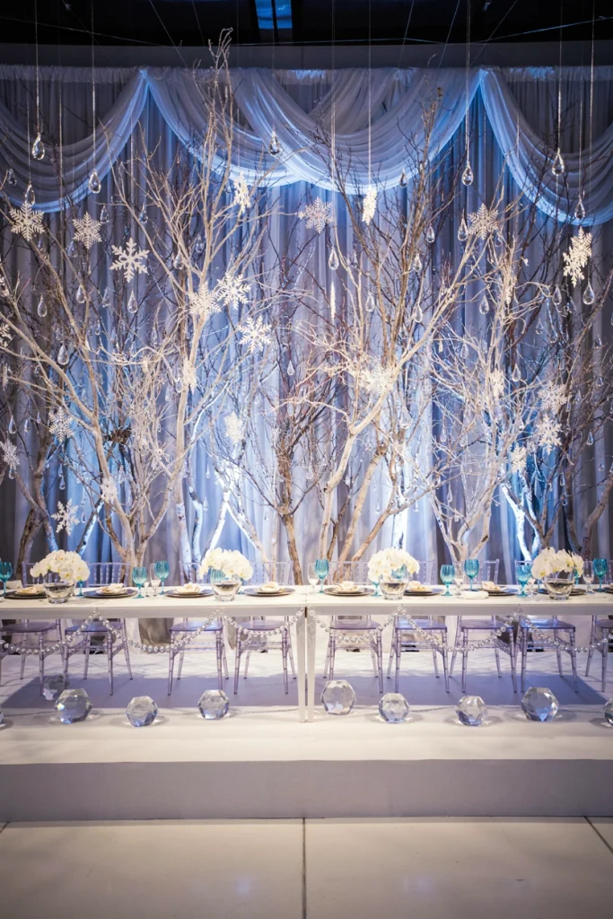 Wedding head table framed by tall frosted white branches hung with crystal pendants