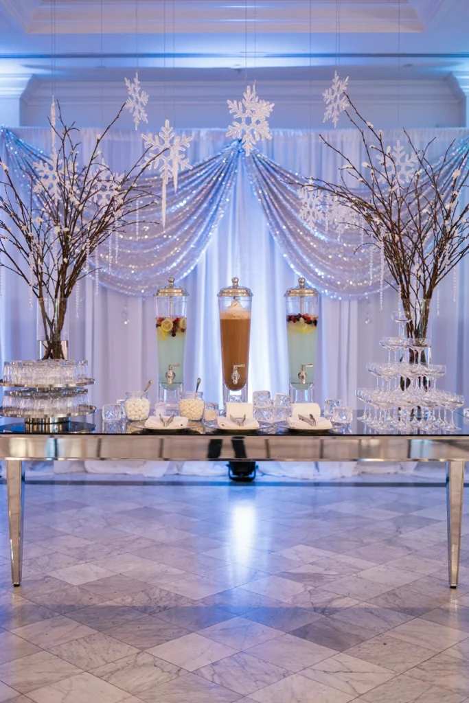 Wedding drink station with a glass beverage dispenser and hot cocoa bar sign styled in silver and white