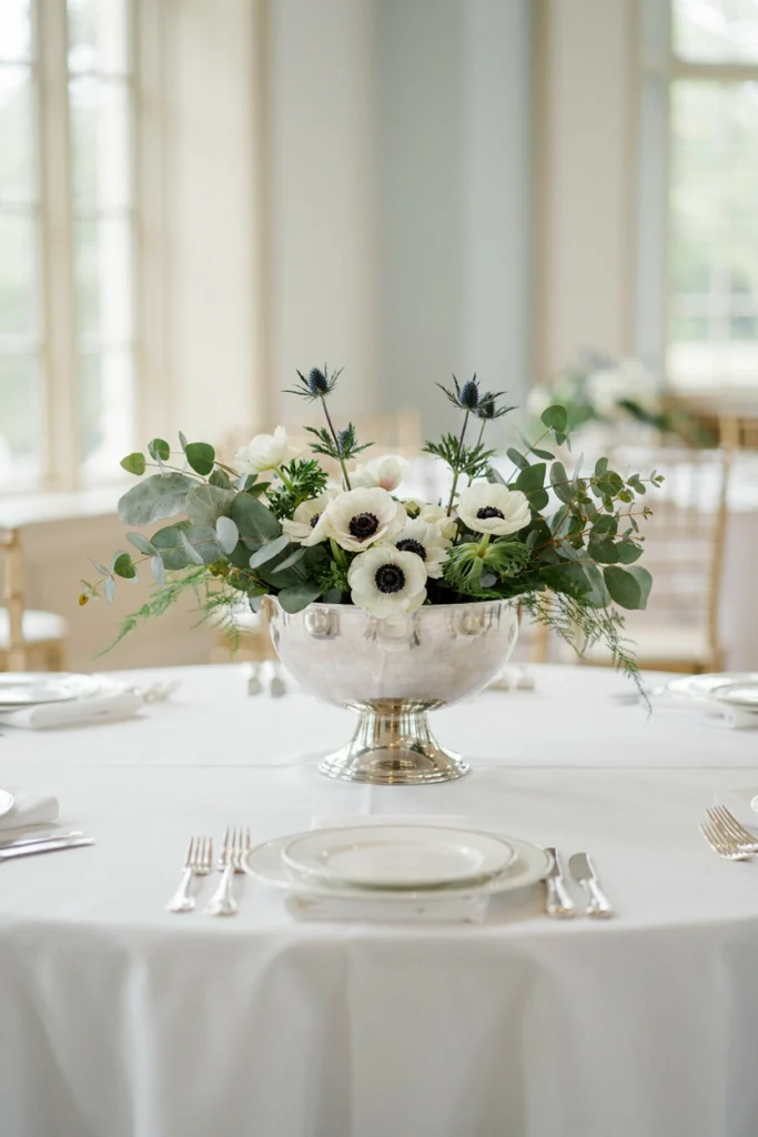 Silver compote vase filled with white anemones, eucalyptus, and blue thistle