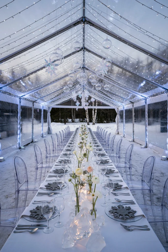 Outdoor winter wedding reception at dusk with string lights and frosted branch centerpieces
