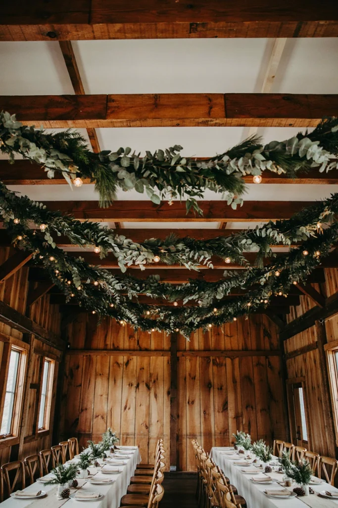 Eucalyptus garland strung along wood ceiling beams above a wedding dinner table